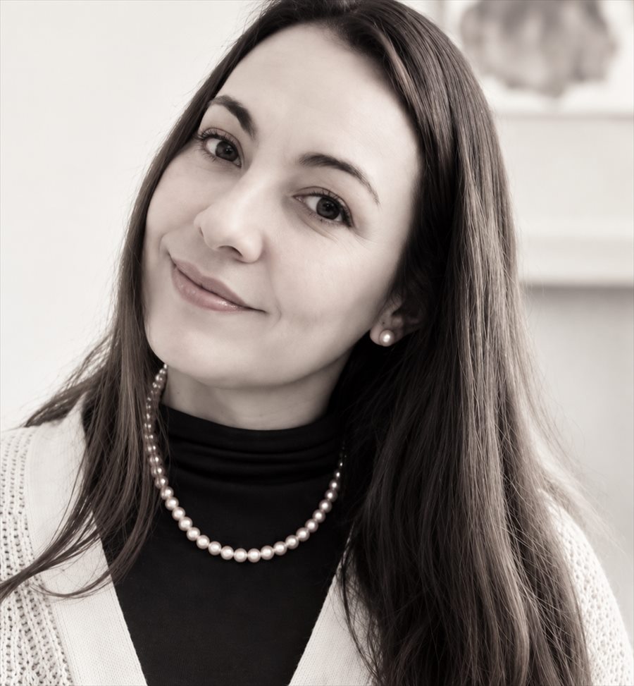 Retrato de Paz en tonos neutros y cálidos, con chaleco claro, suéter negro y collar de perlas, sonriendo a cámara